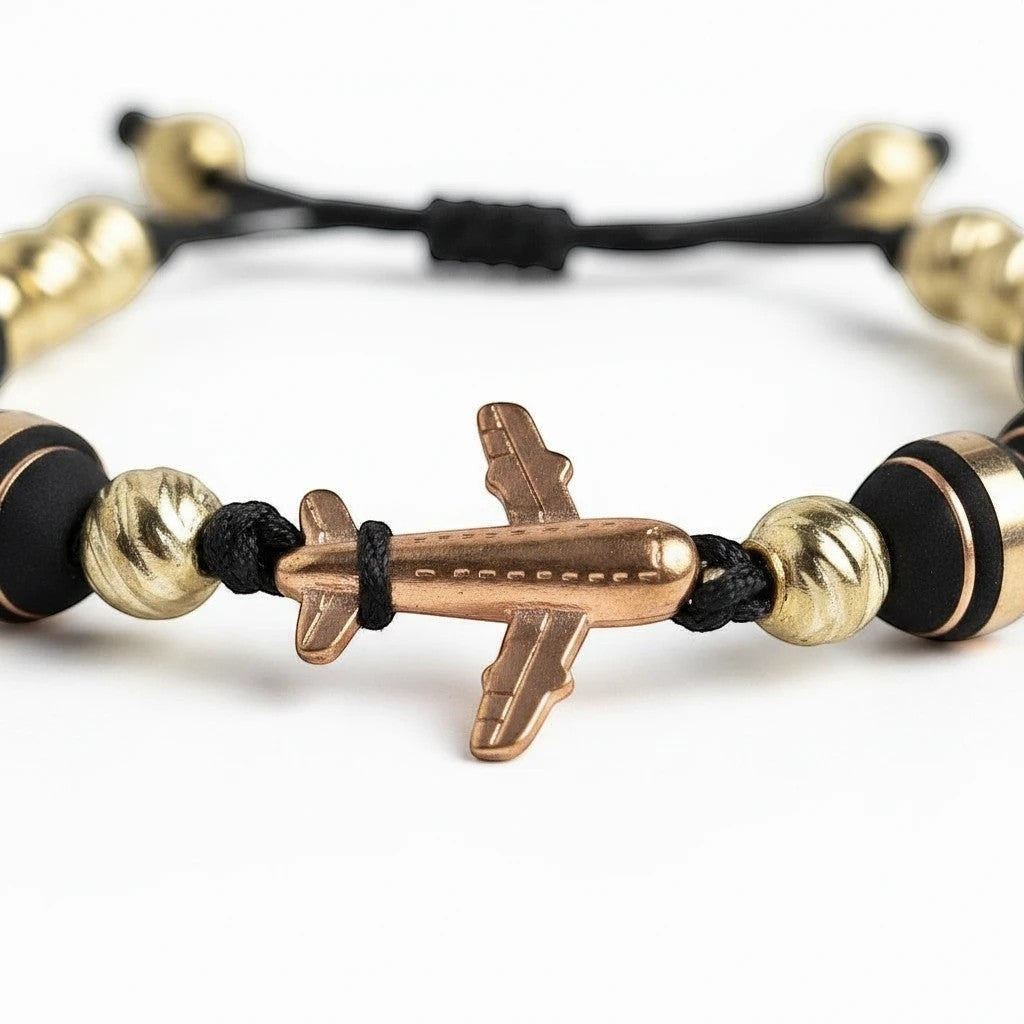 Pulsera ajustable Air Store con abalorios dorados y negros y un dije central de avión metálico para viajeros.